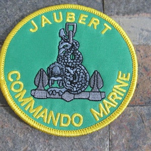 May include: A green and yellow embroidered patch with the text "JAUBERT COMMAND MARINE" and a silver anchor with a snake wrapped around it.