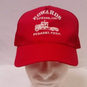 May include: Red trucker hat with a white logo that says "Edwards Express, Inc. Pulaski, Tenn." and a white silhouette of a semi-truck.