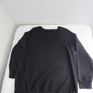 Peut inclure: Un sweat-shirt noir uni avec un col ras du cou et des manches longues. Le sweat-shirt a des poignets et un ourlet c&ocirc;tel&eacute;s. Le v&ecirc;tement est fait d'une mati&egrave;re douce et confortable. Le sweat-shirt est pr&eacute;sent&eacute; sur une surface blanche.