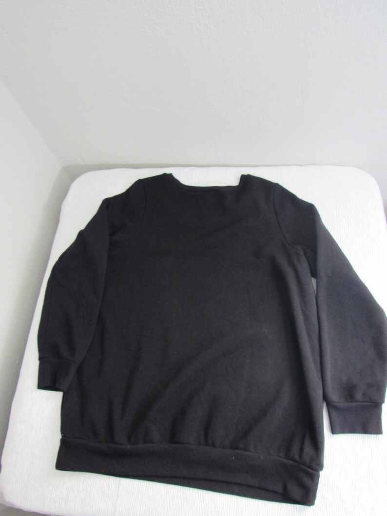 Peut inclure: Un sweat-shirt noir uni avec un col ras du cou et des manches longues. Le sweat-shirt a des poignets et un ourlet c&ocirc;tel&eacute;s. Le v&ecirc;tement est fait d'une mati&egrave;re douce et confortable. Le sweat-shirt est pr&eacute;sent&eacute; sur une surface blanche.