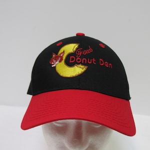May include: Black and red baseball cap with a yellow and red embroidered logo that says "Fred's Donut Den" and a cartoon fox.