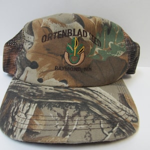 May include: Camouflage trucker hat with the embroidered logo "Ortenblad Seed, Raymond, MN".