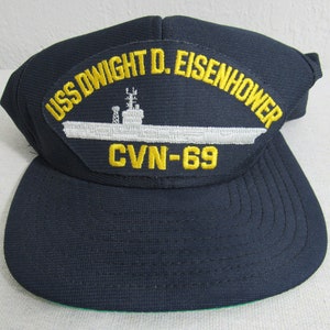 Könnte beinhalten: Eine marineblaue Baseballkappe mit einem gestickten Aufnäher in Weiß und Gelb, auf dem "USS DWIGHT D. EISENHOWER CVN-69" steht.