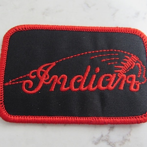 Op de afbeelding: Rood geborduurd "Indian" logo-patch op een zwarte stoffen achtergrond met een rode gestikte rand.