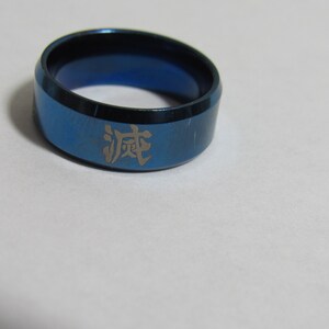 Op de afbeelding: Blauwe ring met zwarte rand en een Japans karakter gegraveerd. De ring is gemaakt van metaal en heeft een gladde, gepolijste afwerking. Een eenvoudig, maar stijlvol accessoire.