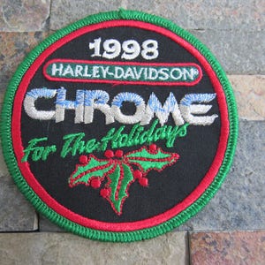 May include: A black, red, and green embroidered patch with the text "1998 Harley-Davidson Chrome For The Holidays".