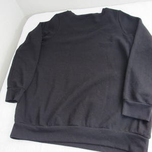 Peut inclure: Un sweat-shirt noir &agrave; manches longues avec un col ras du cou et des poignets et un ourlet c&ocirc;tel&eacute;s. Le sweat-shirt est fait d'un tissu uni et doux. Le v&ecirc;tement est pos&eacute; &agrave; plat sur une surface blanche.