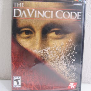 Puede incluir: Caja de juego de PlayStation 2 para el videojuego The Da Vinci Code. La caja presenta un fondo rojo con un primer plano de una pintura de la cara de un hombre. El juego está clasificado como Teen por la ESRB.