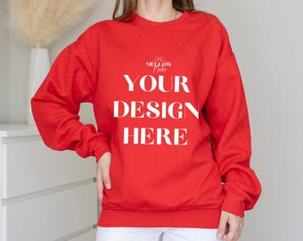 May include: A red sweatshirt with the text "YOUR DESIGN HERE" in white. The sweatshirt is long-sleeved and has a crew neck. The text is centered on the front of the sweatshirt. The sweatshirt is being worn by a person.
