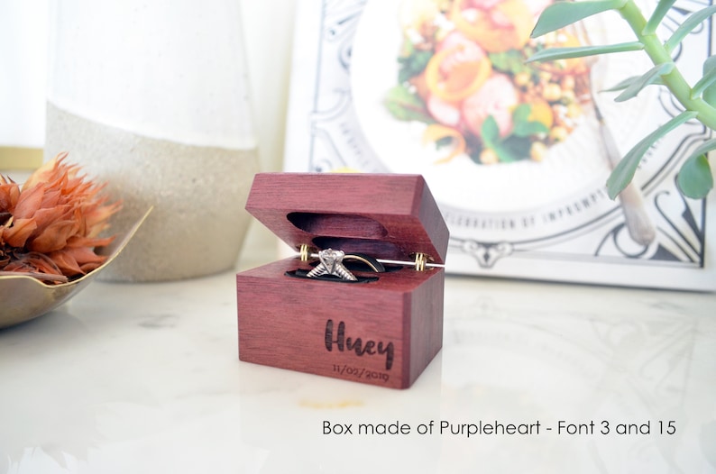 May include: A small wooden ring box made of purpleheart wood with a hinged lid. The box is engraved with the name "Husky" and the date "11/02/2019".