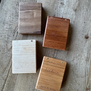 May include: Four rectangular wooden boxes with magnetic closures. Three boxes are plain with varying wood tones including light maple, medium cherry, and dark walnut. One box features engraved text: Matthew 19:6, For Audri, and April 3, 2026.