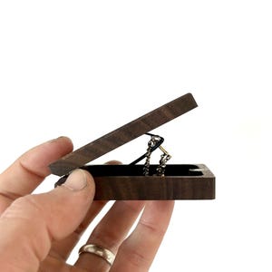May include: A small wooden box with a hinged lid, open to reveal a gold chain necklace inside. The box is made of dark wood with a natural grain pattern.