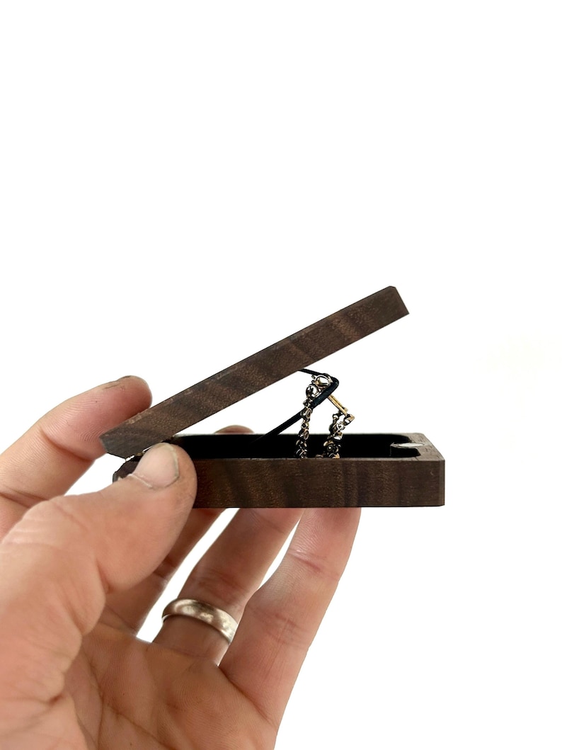 May include: A small wooden box with a hinged lid, open to reveal a gold chain necklace inside. The box is made of dark wood with a natural grain pattern.