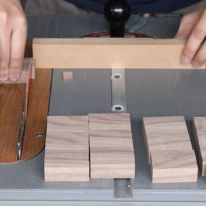 May include: A person using a table saw to cut pieces of wood. The wood is being cut into smaller pieces, and there are several pieces of wood already cut on the table.