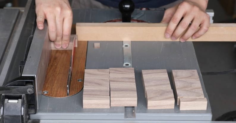 May include: A person using a table saw to cut pieces of wood. The wood is being cut into smaller pieces, and there are several pieces of wood already cut on the table.