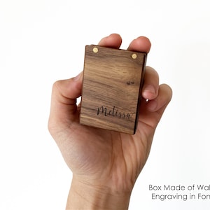 May include: A small wooden box made of walnut with a brass hinge and a personalized inscription that reads "Melissa" in a cursive font. The box is held in a person's hand.