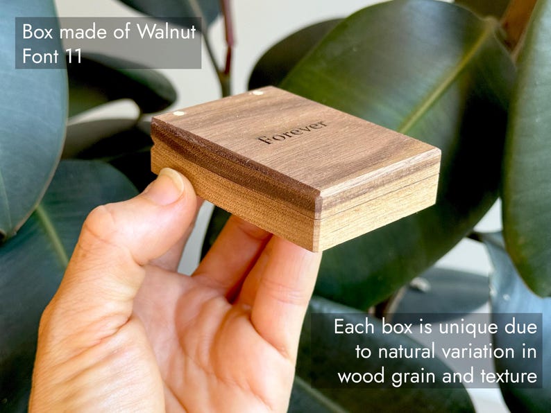 A closed, compact wooden engagement ring box held in hand against a green outdoors background, featuring descriptive text overlays highlighting its solid walnut construction and natural wood grain. Showcasing variation in natural wood grain and color