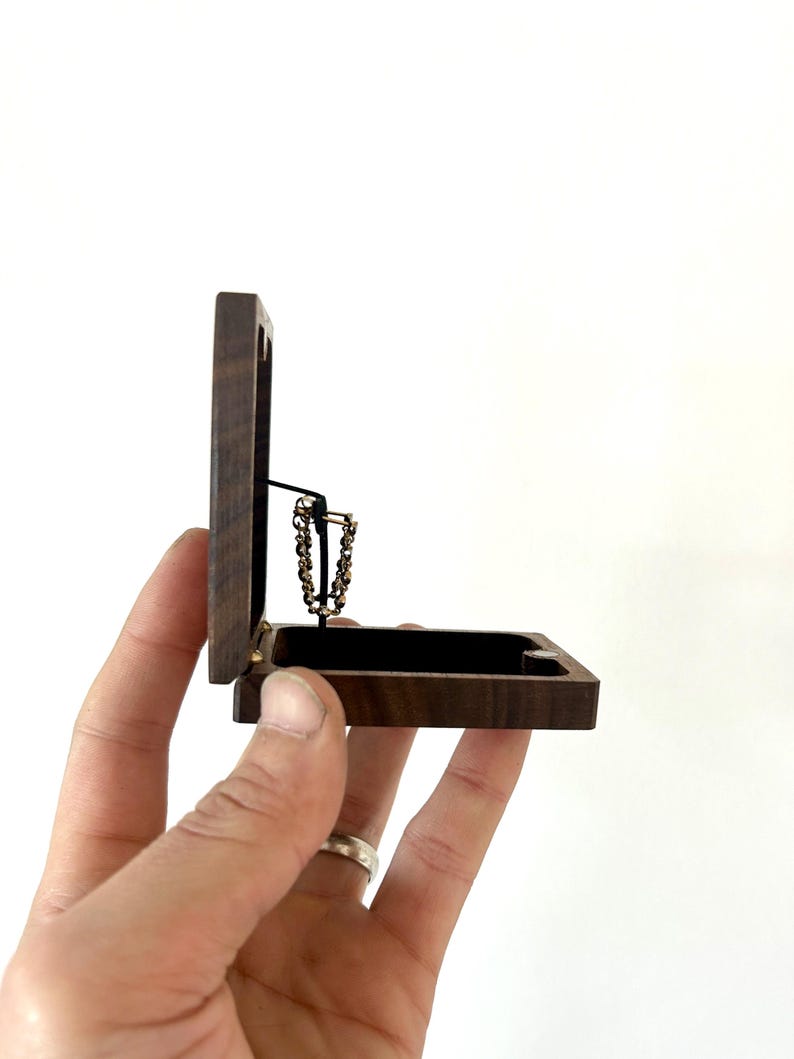 May include: A small wooden box with a hinged lid, open to reveal a gold chain necklace inside. The box is made of dark wood with a natural grain pattern.