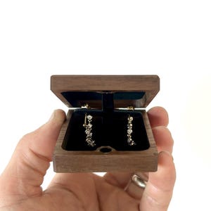 May include: A pair of diamond earrings in a small, dark wood box with a black velvet interior.
