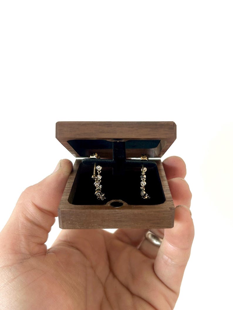 May include: A pair of diamond earrings in a small, dark wood box with a black velvet interior.