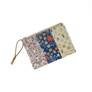 May include: A rectangular zippered pouch with a brown leather pull. The pouch is divided into three vertical sections with different patterns: floral, bear and floral, and rabbit and floral. The colors include beige, blue, brown, and white.