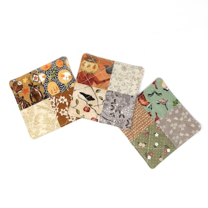 May include: Three square quilted fabric coasters featuring patchwork designs. The patterns include illustrations of pumpkins, birds, floral motifs, and autumn-themed foliage in shades of orange, brown, cream, green, and grey with white cross-stitching.
