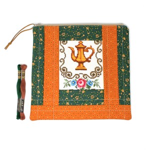 May include: A quilted pouch with a cross-stitched teapot design, featuring orange, green, and white panels. The pouch has a zipper closure and a leather pull. Two spools of embroidery floss in green and brown are next to the pouch.