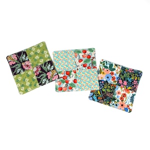 May include: Three square fabric coasters with patchwork designs. One coaster has a green background with floral and leaf patterns. Another has a turquoise background with cherries. The third has a floral pattern with blue and red flowers.