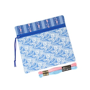 May include: A square zipped pouch featuring a blue and white floral pattern on the main body and a blue striped fabric with small pink flowers at the top. A blue zip pull is attached. Two skeins of embroidery floss, one pink and one light blue.