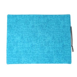 May include: A rectangular, turquoise-colored pouch with a textured fabric appearance. A dark gray drawstring is attached to the side. The pouch is set against a white background.