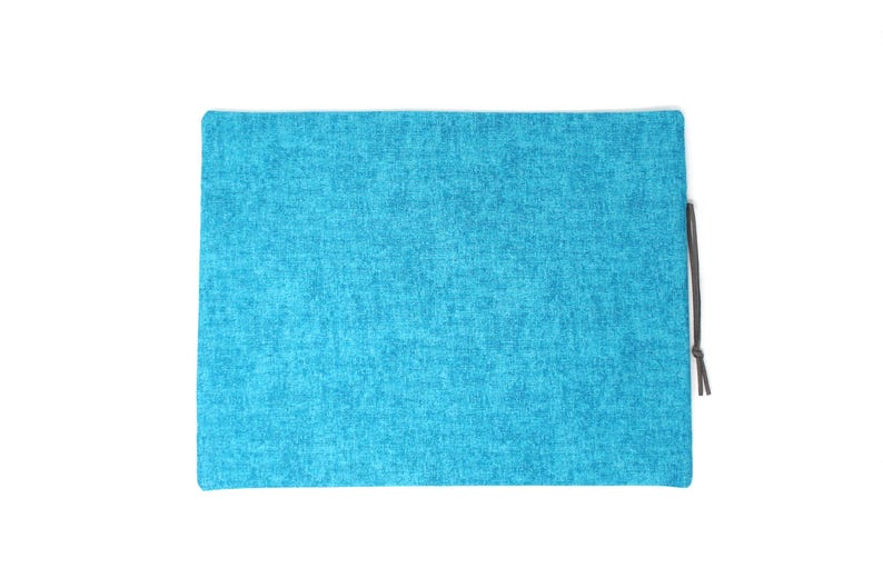 May include: A rectangular, turquoise-colored pouch with a textured fabric appearance. A dark gray drawstring is attached to the side. The pouch is set against a white background.