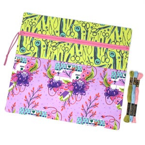 Peut inclure: Un sac de projet de couture rectangulaire avec une fermeture éclair et une tirette roses. La section supérieure a un fond vert citron avec des ciseaux noirs et d'autres outils de couture. La section inférieure a un fond lavande avec un motif floral et de machine à coudre. Trois échevettes de fil à broder sont à droite.