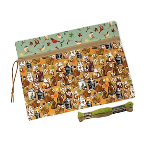May include: A rectangular zipped pouch featuring a pattern of maple syrup jugs and autumn leaves on a mustard yellow background, with a sage green top border displaying birds and leaves, accompanied by two skeins of green and brown embroidery floss.