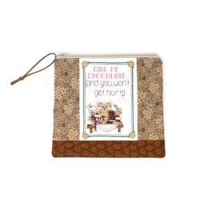May include: A square, zipped pouch with a brown floral pattern and a brown leather pull. The centre features a cross-stitch design with the text "GIVE ME CHOCOLATE (and you won't get hurt!)" and a teddy bear.