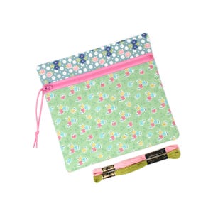 May include: A square, floral-patterned pouch with a pink zip and drawstring, and two skeins of embroidery thread. The pouch has a green background with a repeating pattern of small flowers. The zip is pink, and the drawstring is a matching pink.