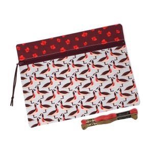 May include: A rectangular zipped pouch featuring a repeating pattern of Canada geese on a light grey background, with a dark maroon top border decorated with red maple leaves. Two skeins of embroidery floss in red and brown are included.