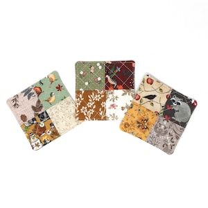 May include: Three square fabric coasters featuring a quilted diamond pattern. Each coaster is composed of four distinct patches with various prints, including birds, a raccoon, floral motifs, leaves, and autumn-themed patterns in earth tones.