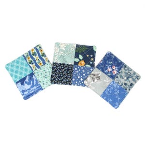 May include: Three square fabric coasters featuring a patchwork design of various blue, white, and green floral and geometric patterns. The quilted squares display motifs including small flowers, stars, and a squirrel illustration on a blue background.