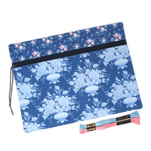 May include: A rectangular fabric pouch featuring a dark blue floral print with light blue vases and flowers, accented by a top strip of dark blue fabric with a small pink rose pattern. A dark zip closure is present, along with two embroidery floss skeins.