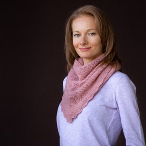 Könnte beinhalten: Eine Frau trägt einen hellrosa gestrickten Schal mit einem weißen Pullover.