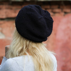 May include: A black knitted beanie with a slouchy fit. The beanie is made of a soft, textured yarn.