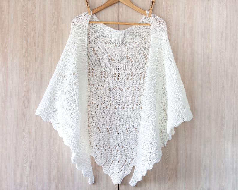 May include: White crocheted shawl with a delicate lace pattern hanging on a wooden hanger.