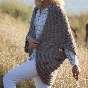 May include: A brown knitted cardigan with a draped, open front and long sleeves. The cardigan is made of a soft, textured yarn and has a relaxed fit.