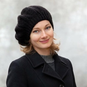 May include: A black knitted beret with a ribbed texture and a rounded crown. The hat is constructed from thick yarn and features a soft, slouchy silhouette that sits comfortably on the head, providing full coverage with a classic, simple design.