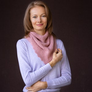 K&ouml;nnte beinhalten: Ein hellrosa gestrickter Schal wird um den Hals getragen. Der Schal ist aus einem weichen, strukturierten Garn gefertigt. Die Person tr&auml;gt ein hellviolettes Langarmshirt. Der Hintergrund ist einfarbig dunkelbraun.