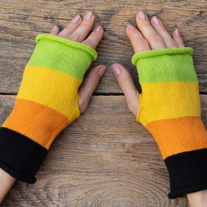 Peut inclure: Une paire de mitaines colorées. Les gants présentent des rayures horizontales vertes, jaunes, oranges et noires. Fabriqués en tricot, ils sont conçus pour garder les mains au chaud tout en laissant les doigts libres.