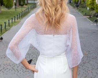 Puede incluir: Un top bolero blanco transparente de manga larga, combinado con un vestido blanco a juego. El bolero presenta un tejido delicado y abierto, y el vestido tiene un diseño elegante y ajustado. El conjunto es adecuado para ocasiones especiales.
