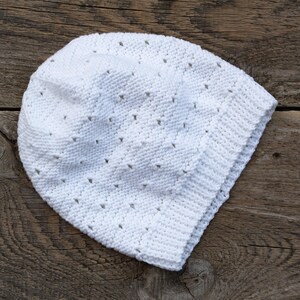 May include: A white crocheted hat with a lacy pattern. The hat is lying on a wooden surface.