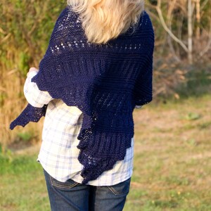 May include: A navy blue knitted shawl with a lacy pattern. The shawl is draped over the shoulders of a person wearing a plaid shirt and blue jeans.