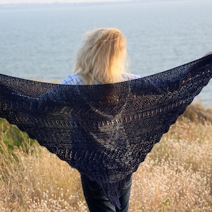 Könnte beinhalten: Ein dunkelblauer gestrickter Schal mit einem Spitzenmuster, getragen von einer Person, die in einem Feld mit hohem Gras steht.